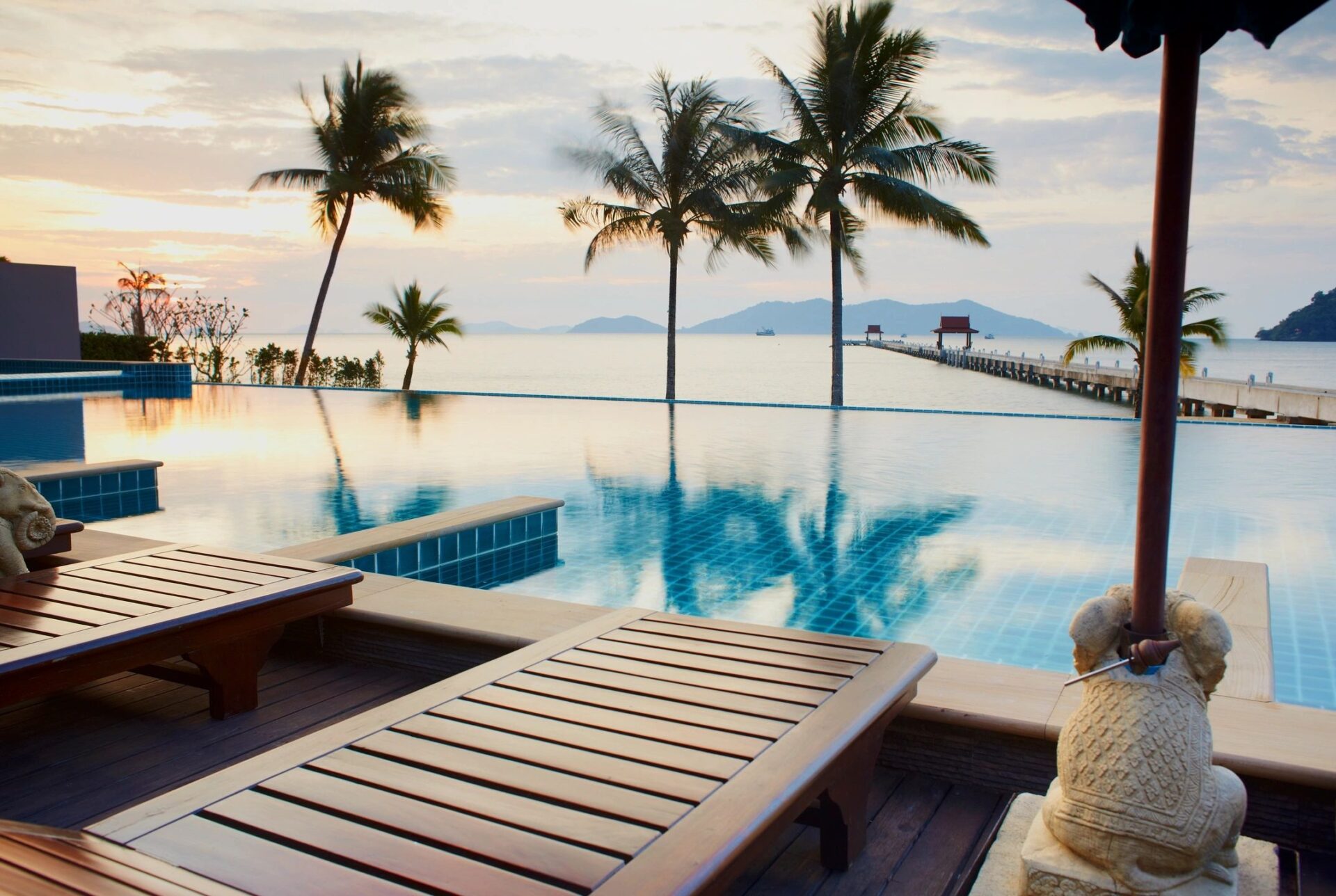 A pool with wooden benches and palm trees in the background.
